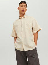 رجل يرتدي قميص نص كم رجالي بيج فاتح مع بنطال رمادي