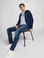 رجل يجلس على كرسي مرتديًا بنطلون جينز سليم فيت أزرق داكن مع سترة كحلية وحذاء أبيض.