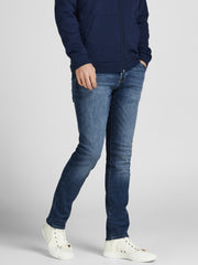 رجل يرتدي بنطلون جينز سليم فيت أزرق داكن مع سترة كحلية وتيشيرت أبيض وحذاء رياضي أبيض.