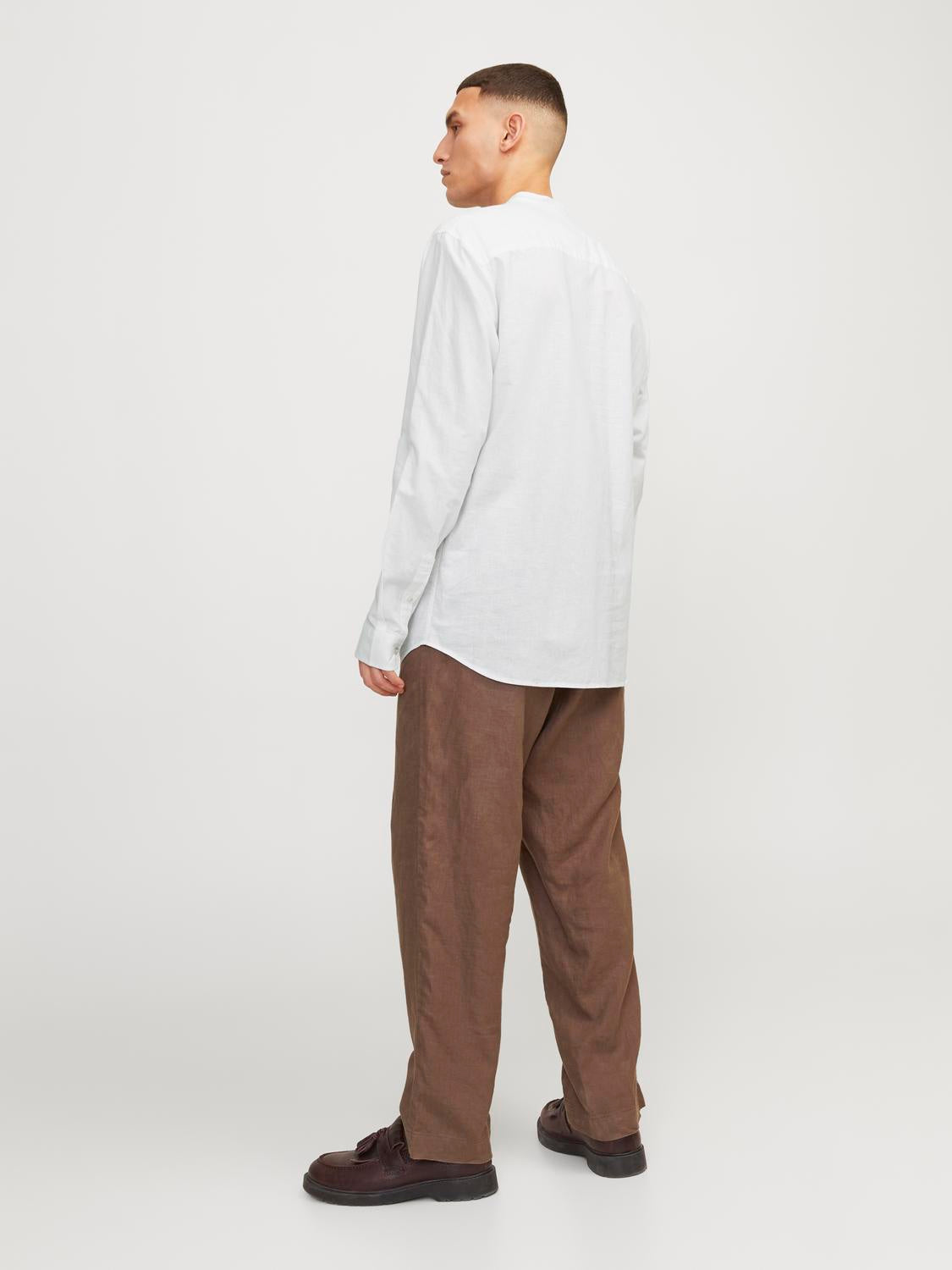  رجل يرتدي قميص رجالي أبيض بأكمام طويلة وقصّة مريحة، يظهر من الجانب مع بنطال بني داكن.