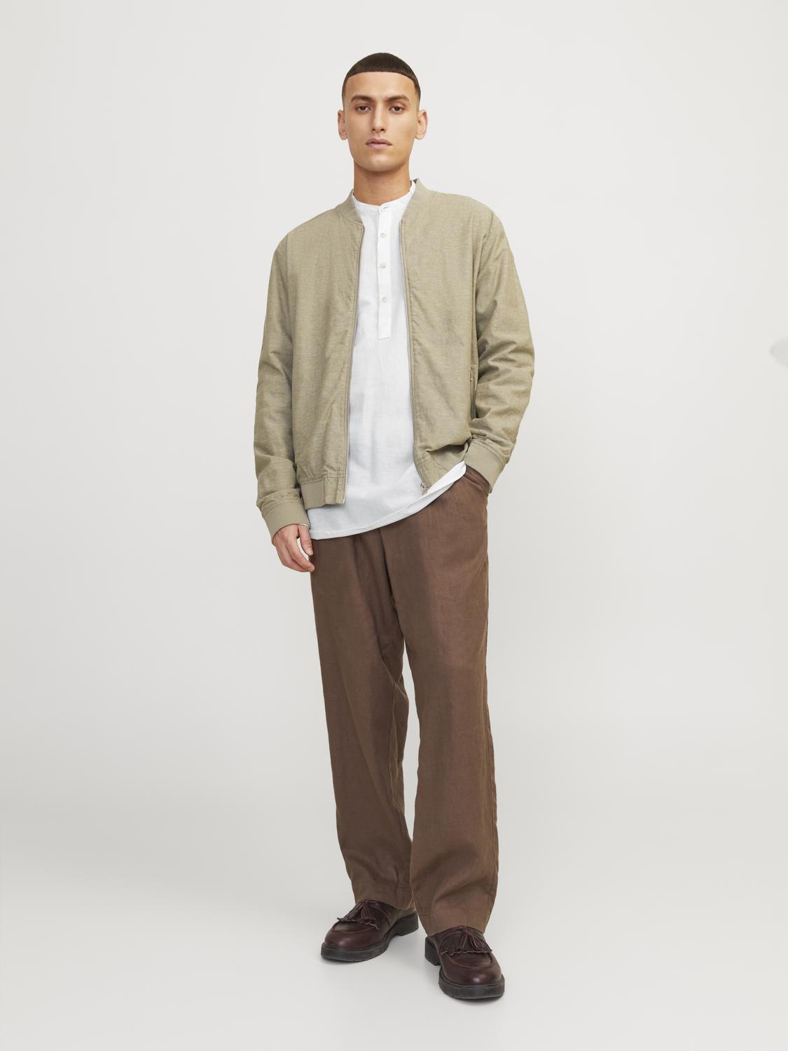 رجل يرتدي قميص رجالي أبيض بأكمام طويلة تحت سترة بيج، مع بنطال بني، يقف في وضعية أنيقة.