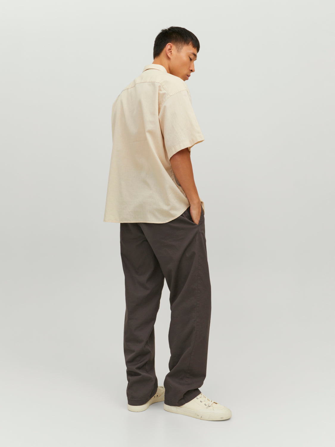 رجل يرتدي قميص نص كم بيج فاتح وبنطال رمادي، يظهر من زاوية جانبية
