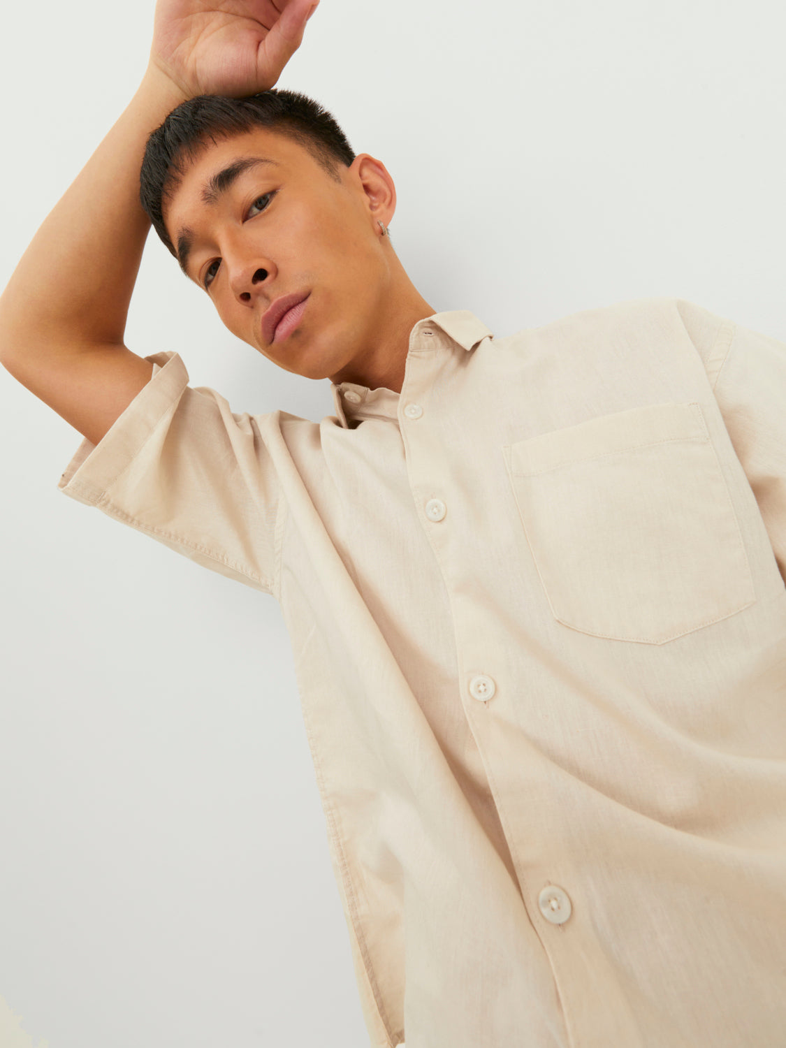  رجل يرتدي قميص نص كم بيج فاتح يرفع يده إلى رأسه في لقطة عفوية